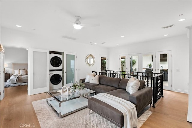 living room featuring light wood-type flooring, ceiling fan, stacked washer / dryer, and french doors