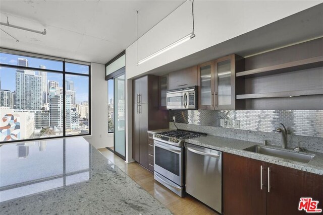 kitchen with tasteful backsplash, sink, light hardwood / wood-style flooring, stainless steel appliances, and light stone counters