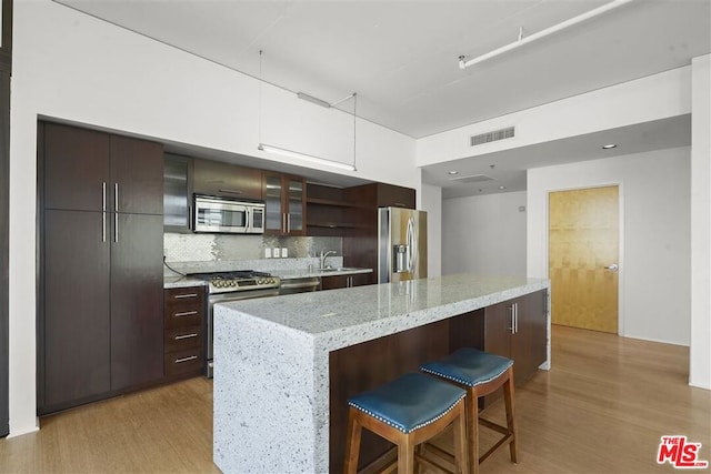 kitchen featuring a breakfast bar area, stainless steel appliances, tasteful backsplash, a kitchen island, and dark brown cabinetry