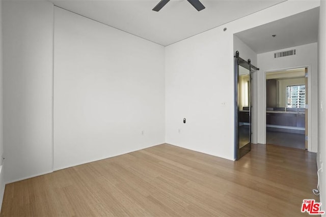 empty room with ceiling fan, a barn door, and hardwood / wood-style floors