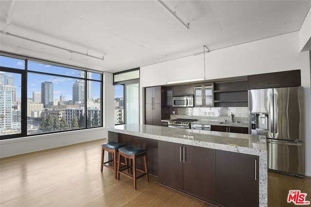 kitchen with stainless steel appliances, backsplash, light stone counters, dark brown cabinetry, and sink