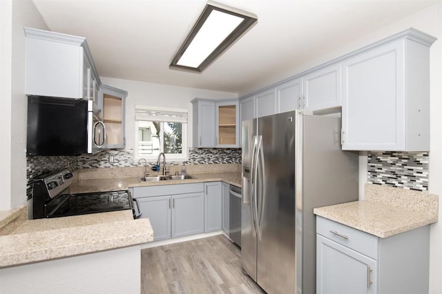 kitchen with tasteful backsplash, sink, light wood-type flooring, appliances with stainless steel finishes, and light stone counters