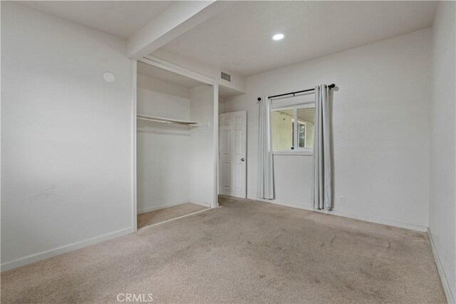 unfurnished bedroom with a closet, light carpet, and beamed ceiling