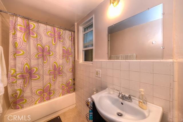 bathroom with backsplash, tile walls, shower / bath combo with shower curtain, and sink