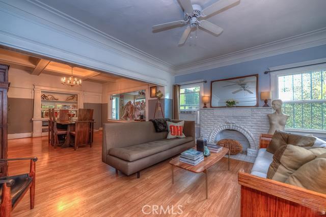 living room with ceiling fan with notable chandelier, light wood-type flooring, ornamental molding, and a brick fireplace