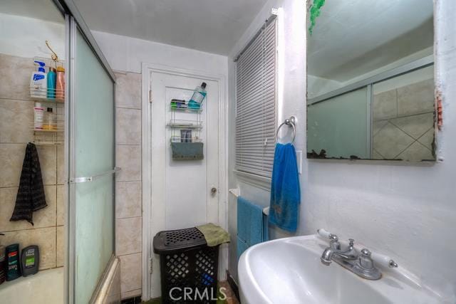 bathroom with sink and bath / shower combo with glass door