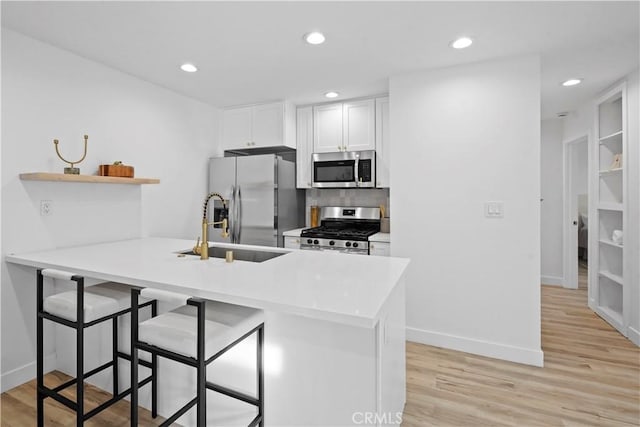 kitchen featuring kitchen peninsula, sink, appliances with stainless steel finishes, a kitchen breakfast bar, and white cabinets