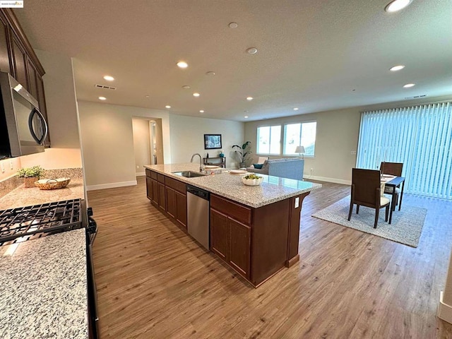 kitchen with stainless steel appliances, a kitchen island with sink, light stone countertops, light hardwood / wood-style flooring, and sink