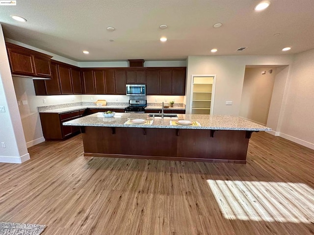 kitchen with stainless steel appliances, light hardwood / wood-style flooring, light stone counters, and sink