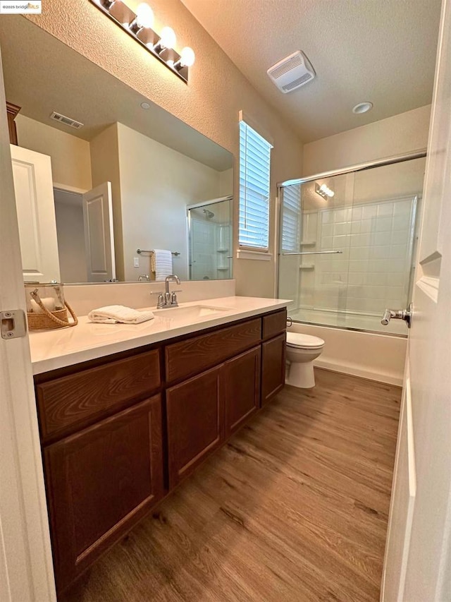 full bathroom with toilet, wood-type flooring, a textured ceiling, vanity, and shower / bath combination with glass door