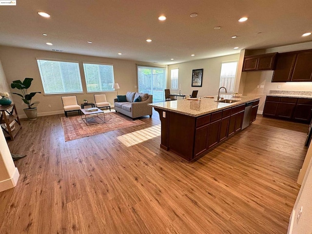 kitchen with dishwasher, sink, a kitchen island with sink, light wood-type flooring, and light stone counters