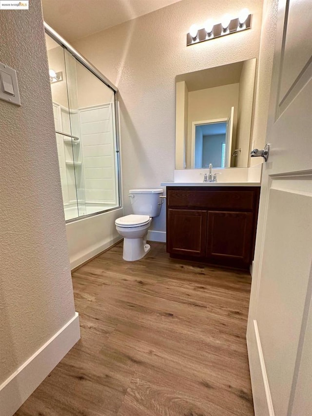 full bathroom with bath / shower combo with glass door, wood-type flooring, toilet, and vanity