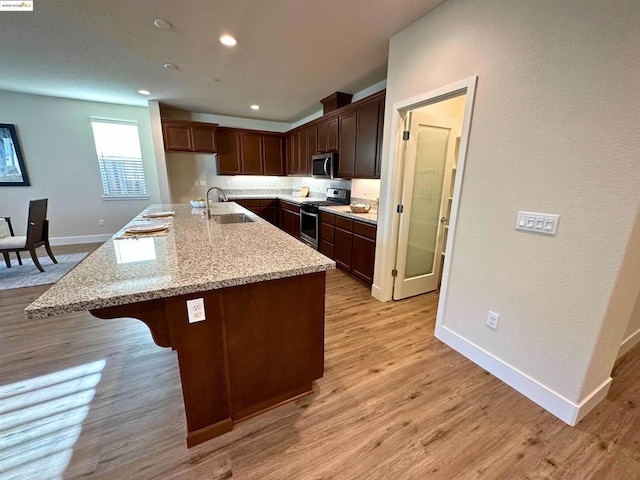 kitchen featuring appliances with stainless steel finishes, light hardwood / wood-style flooring, sink, light stone counters, and a center island with sink