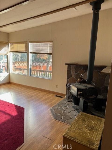 living room with beam ceiling, a wood stove, and wood-type flooring