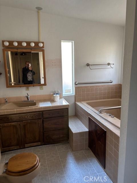 bathroom with vanity, toilet, and a relaxing tiled tub