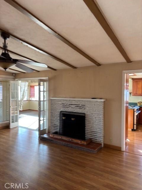 unfurnished living room with hardwood / wood-style floors, a stone fireplace, ceiling fan, vaulted ceiling with beams, and french doors