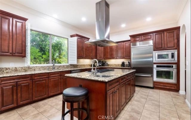 kitchen with a kitchen bar, island exhaust hood, built in appliances, sink, and a kitchen island with sink