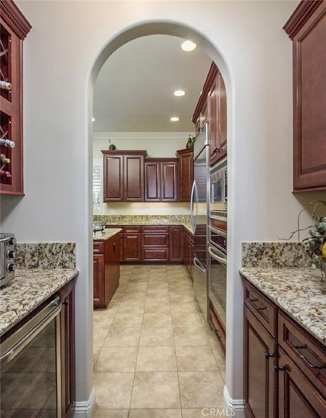 kitchen with crown molding, stainless steel appliances, light tile patterned floors, beverage cooler, and light stone counters