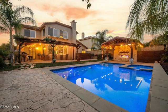 pool at dusk with an in ground hot tub, exterior bar, a patio, and a fireplace