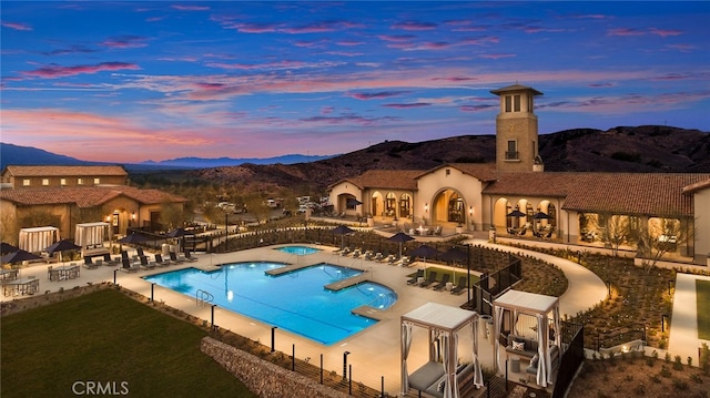 pool at dusk with a mountain view, a community hot tub, and a patio area