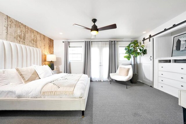 carpeted bedroom with ceiling fan, multiple windows, and a barn door