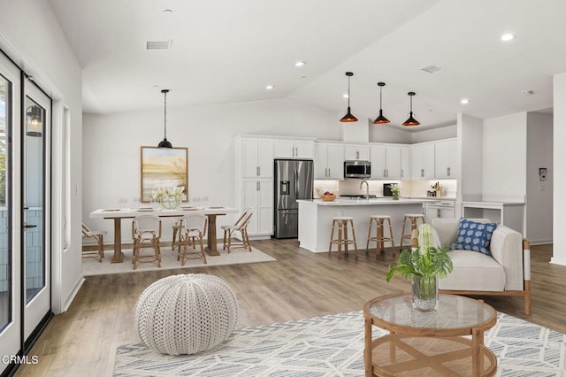 living room featuring light wood-type flooring, vaulted ceiling, and sink