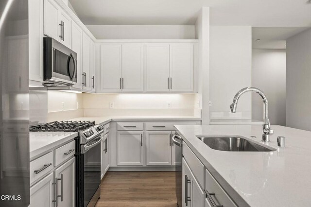 kitchen with appliances with stainless steel finishes, sink, white cabinetry, and dark hardwood / wood-style floors