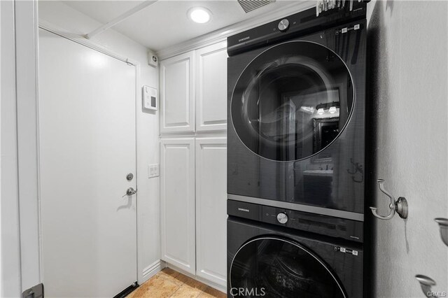 laundry area with stacked washing maching and dryer and cabinets