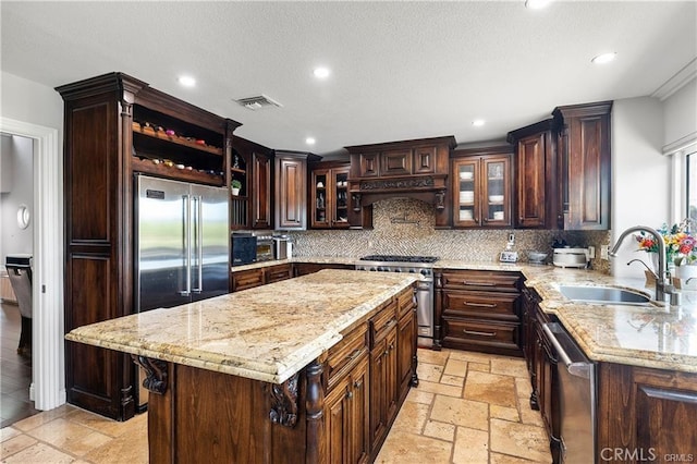 kitchen with dark brown cabinetry, a kitchen island, high end appliances, decorative backsplash, and sink