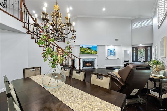 dining space with plenty of natural light, a premium fireplace, a chandelier, a towering ceiling, and ornamental molding