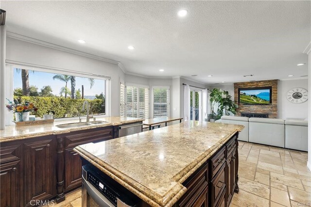 kitchen featuring light stone countertops, a kitchen island, crown molding, stainless steel dishwasher, and sink