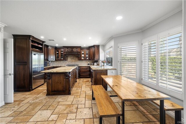 kitchen featuring a kitchen island, stainless steel appliances, decorative backsplash, ornamental molding, and dark brown cabinets