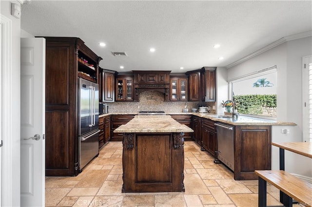 kitchen with appliances with stainless steel finishes, backsplash, a center island, dark brown cabinets, and sink