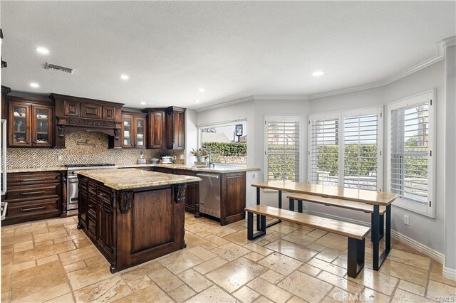 kitchen featuring appliances with stainless steel finishes, tasteful backsplash, custom range hood, a kitchen island, and dark brown cabinetry