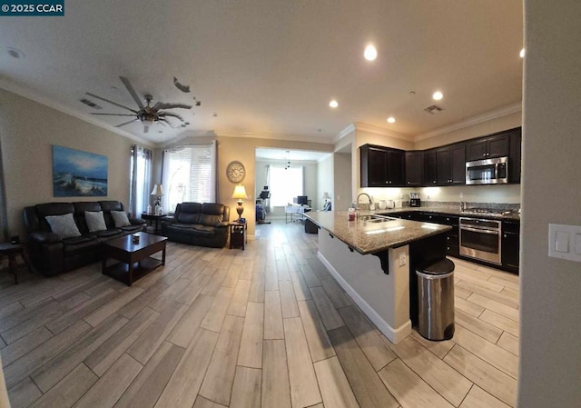 kitchen with appliances with stainless steel finishes, a kitchen breakfast bar, light stone countertops, crown molding, and sink