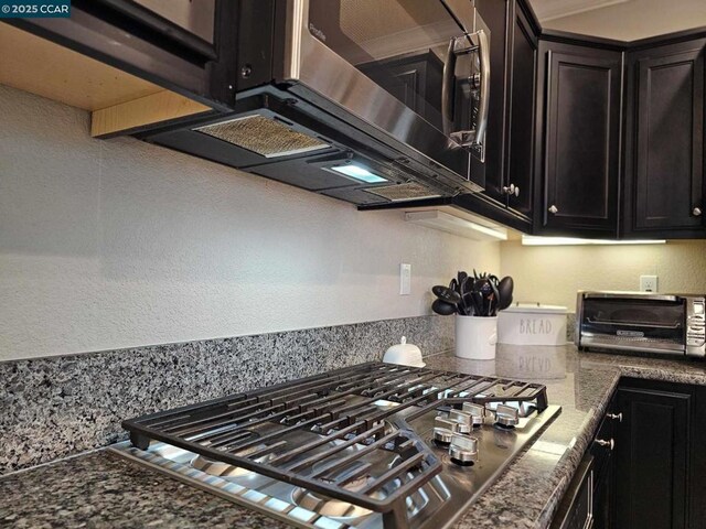 kitchen with appliances with stainless steel finishes, dark stone counters, and dark brown cabinets