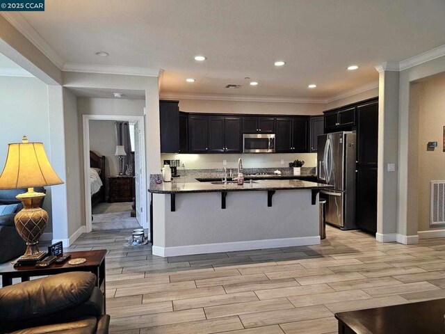 kitchen with stainless steel appliances, kitchen peninsula, light stone counters, crown molding, and a breakfast bar area