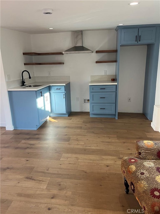 kitchen with sink, light wood-type flooring, wall chimney range hood, and blue cabinets