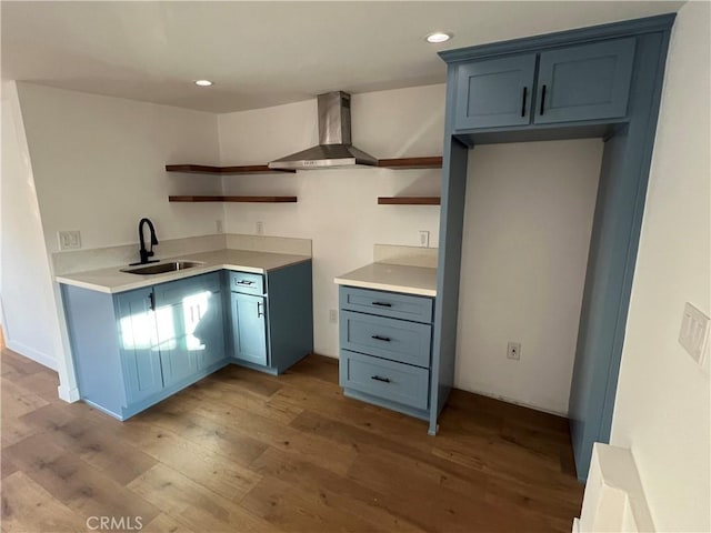 kitchen with blue cabinetry, wall chimney range hood, sink, and light hardwood / wood-style flooring