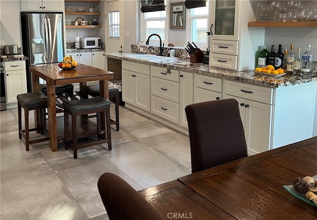 kitchen with sink, dark stone counters, white cabinets, and stainless steel refrigerator with ice dispenser