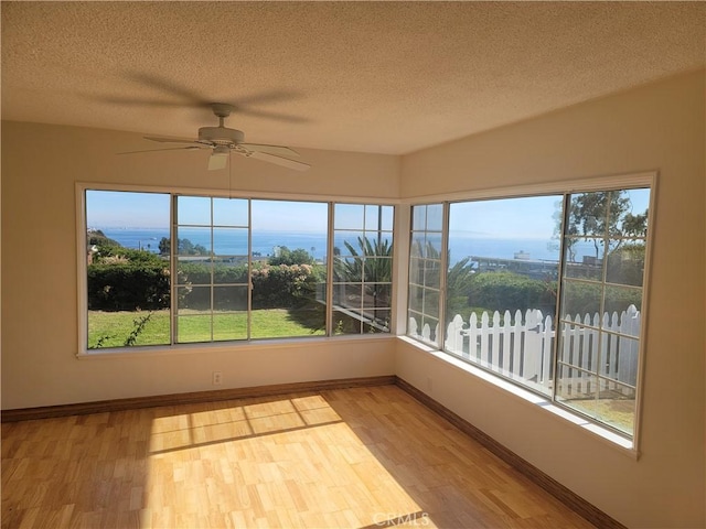 unfurnished sunroom featuring ceiling fan and a water view