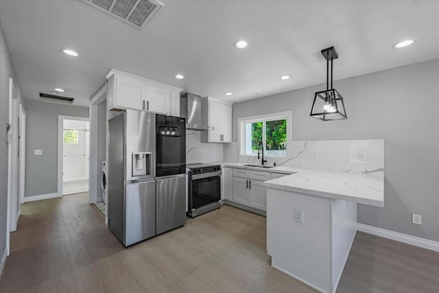 kitchen featuring kitchen peninsula, stainless steel appliances, wall chimney range hood, white cabinets, and sink