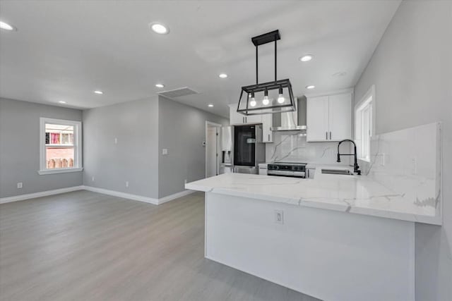 kitchen with pendant lighting, kitchen peninsula, sink, stainless steel appliances, and wall chimney exhaust hood