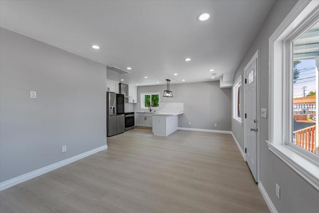 kitchen with hanging light fixtures, stainless steel fridge, white cabinetry, and light hardwood / wood-style floors