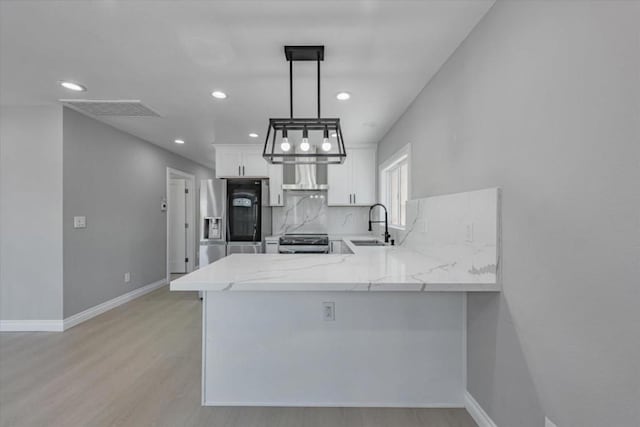 kitchen with appliances with stainless steel finishes, decorative light fixtures, white cabinetry, kitchen peninsula, and range hood