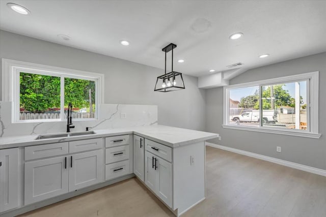 kitchen with white cabinetry, kitchen peninsula, light stone countertops, pendant lighting, and sink