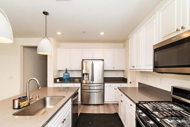 kitchen featuring appliances with stainless steel finishes, white cabinetry, sink, hanging light fixtures, and light hardwood / wood-style flooring