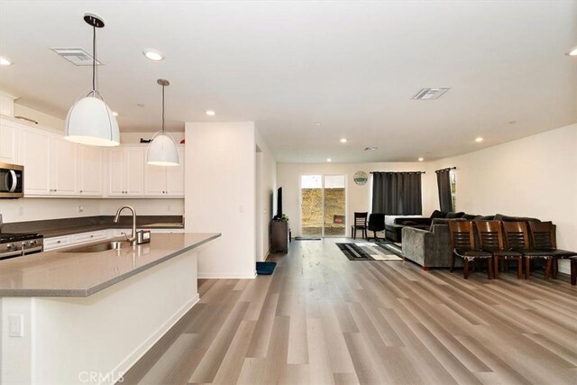 kitchen with white cabinets, light hardwood / wood-style floors, stainless steel appliances, hanging light fixtures, and sink