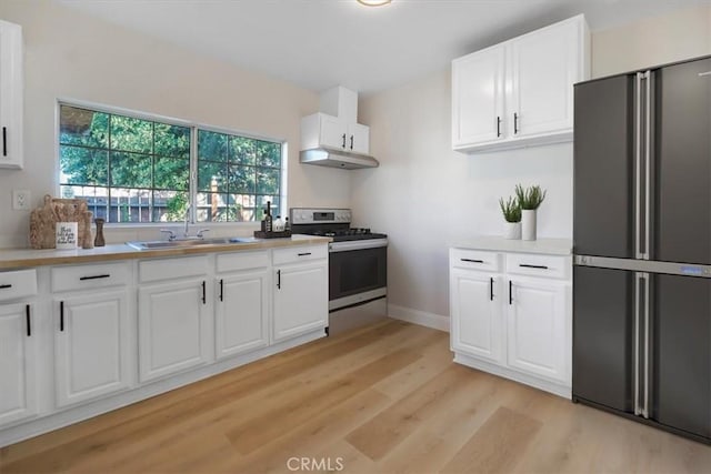 kitchen with white cabinets, sink, light wood-type flooring, fridge, and stainless steel range oven