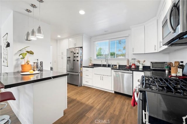 kitchen featuring dark hardwood / wood-style floors, pendant lighting, sink, white cabinetry, and stainless steel appliances